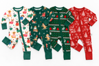 Four baby long-sleeve footless onesies arranged side by side on a white background, each with a different Christmas print: white with dog illustrations, dark green with dog and tree motifs, dark green with reindeer and tree patterns, and red with reindeer and tree patterns.