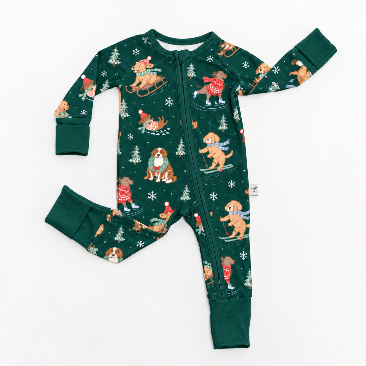 A long-sleeve baby footed one-piece pajama in dark green, featuring an all-over print of dogs sledding and skiing during winter with snowflakes, set against a plain white background.