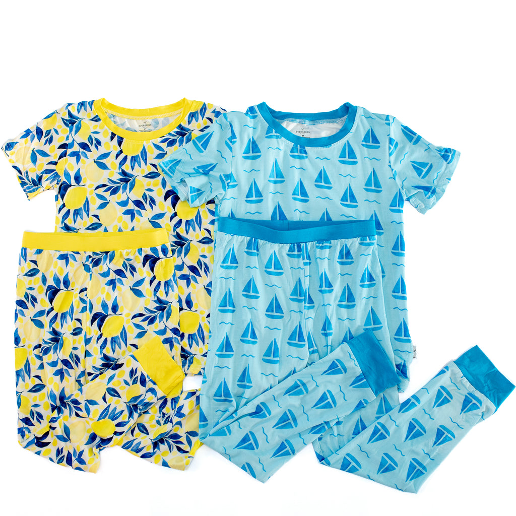 Two children's short-sleeve pajama sets laid flat on a white background. The left set is yellow with blue leaf and lemon prints and a yellow waistband.