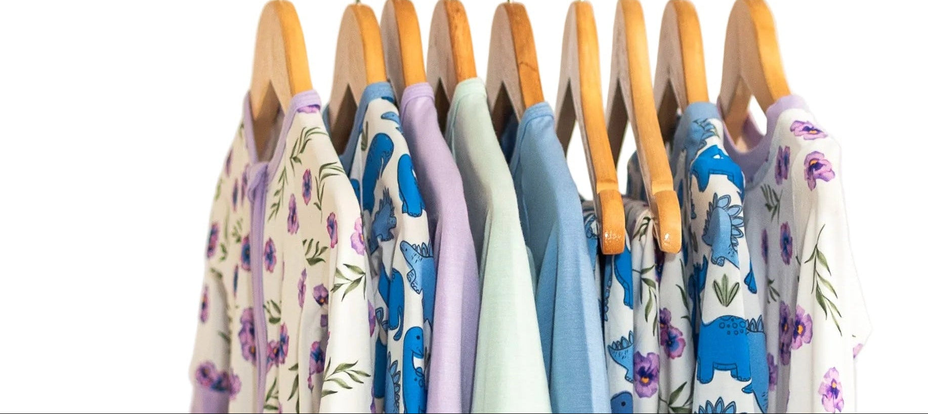 Children's clothing with dinosaur patterns on hangers against a white wall