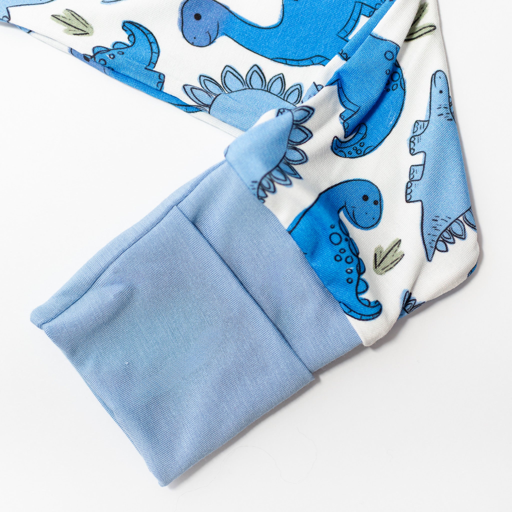 Pattern of blue dinosaurs on white bamboo fabric pajamas with cuff hands.