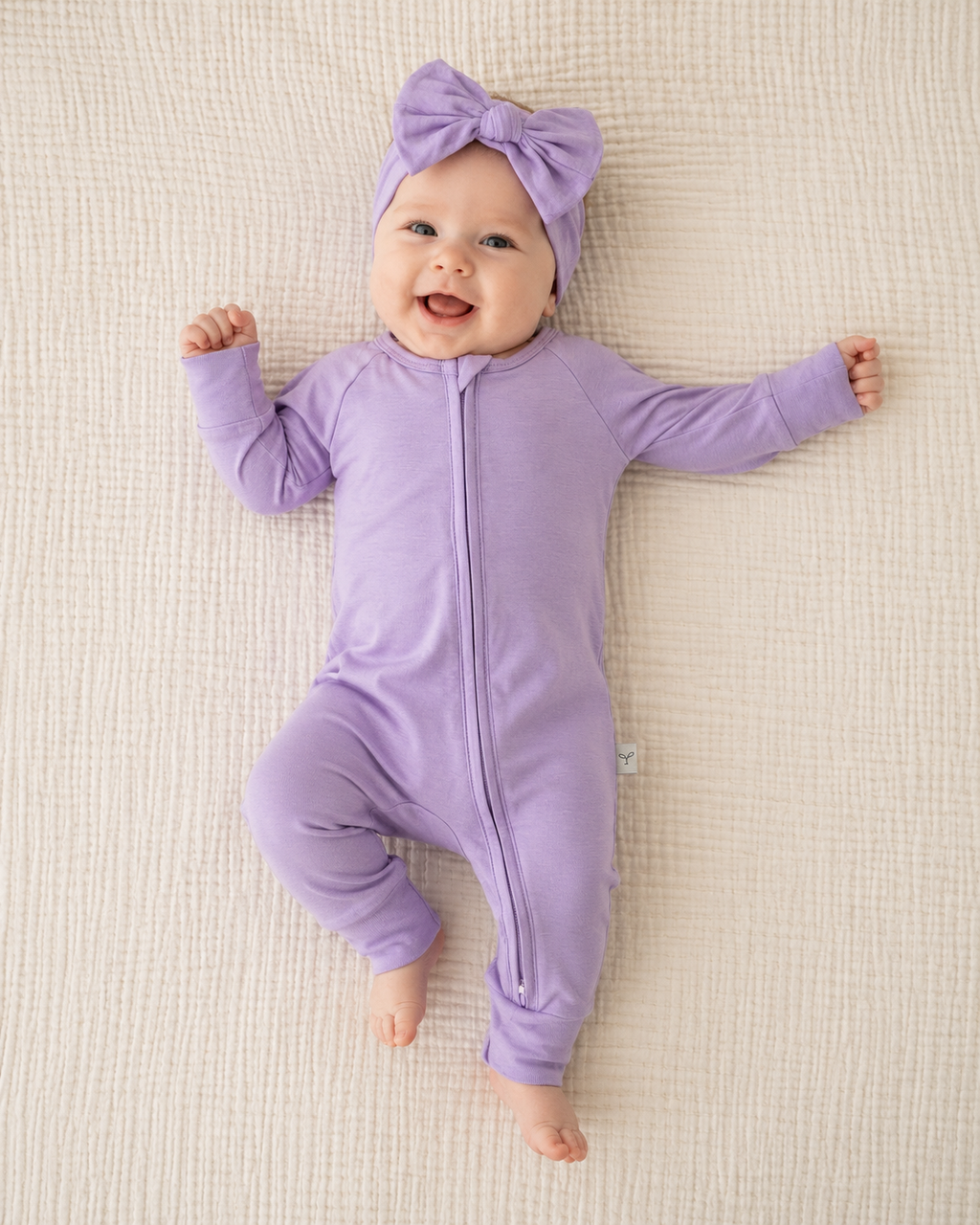 Baby in a purple outfit with a matching headband on a beige blanket