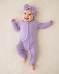 Baby in a purple outfit with a matching headband on a beige blanket