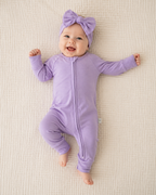 Baby in a purple outfit with a matching headband on a beige blanket