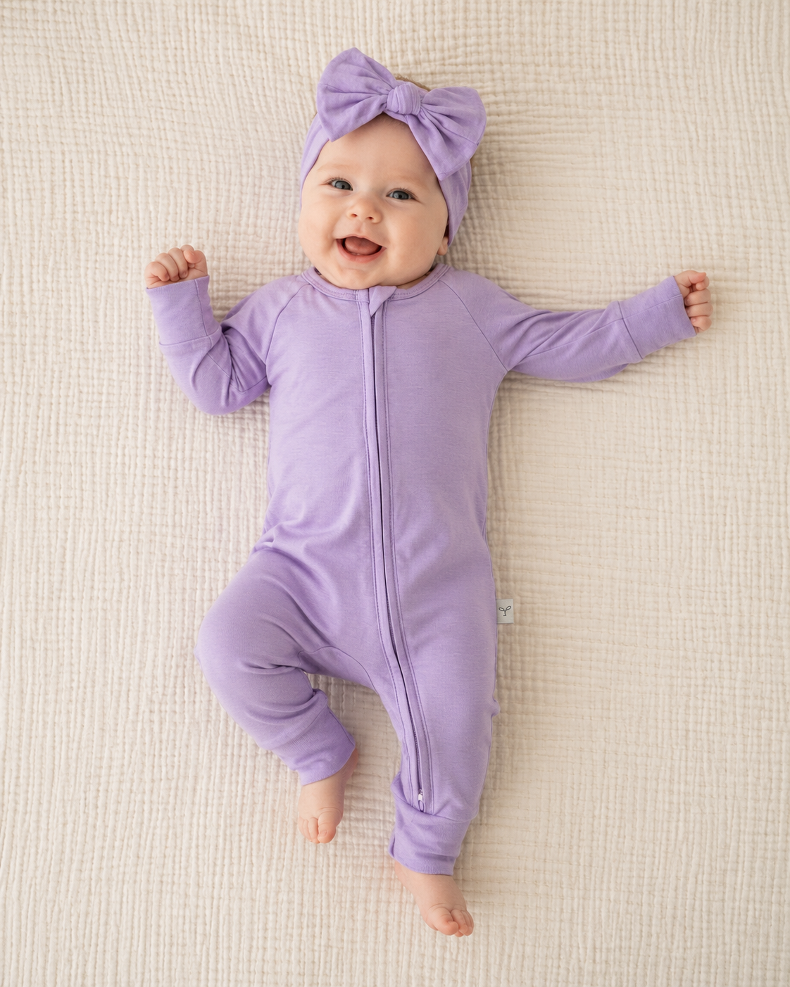 Baby in a purple outfit with a matching headband on a beige blanket